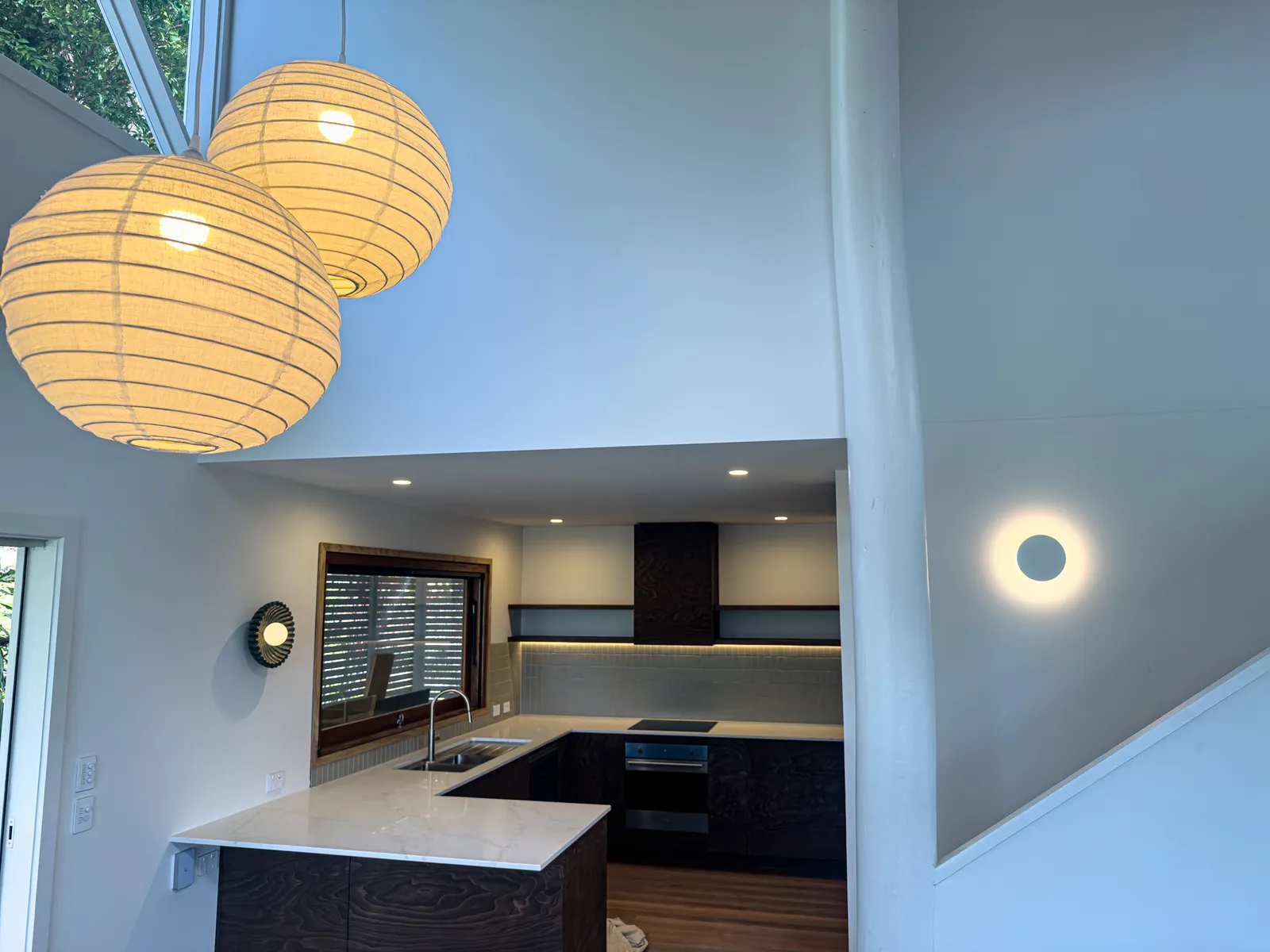 Two large paper globe pendants hanging in a double height kitchen, with downlights and a round wall light.